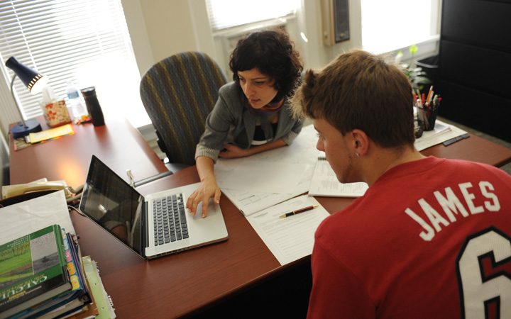 Two people sitting at a desk looking at a laptop Two people sitting at a desk looking at a laptop
