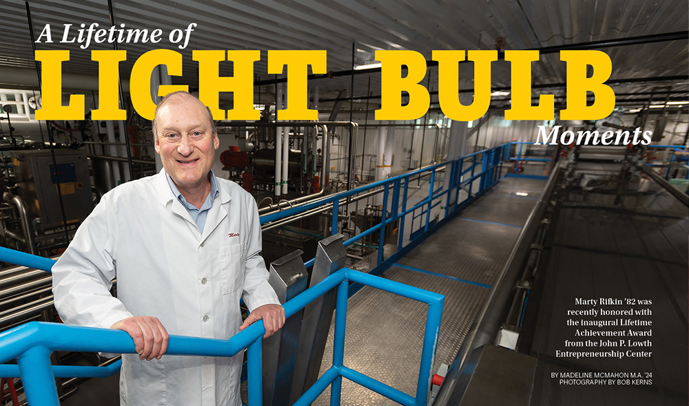 A MAN IN A WHITE LAB COAT STANDING IN A MANUFACURING PLANT.