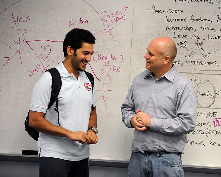 Professor and student talking near the front of the classroom.