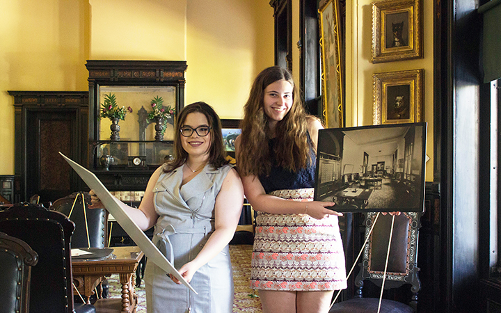 Two students stand in the Henry B. Plant Museum holding museum material.